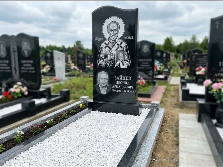 Памятник с гравировкой иконы: стела с крестообразным навершием — икона в резной рамке-киоте, газон без ограды, стриженая трава, работа «Раевская» в Омске
