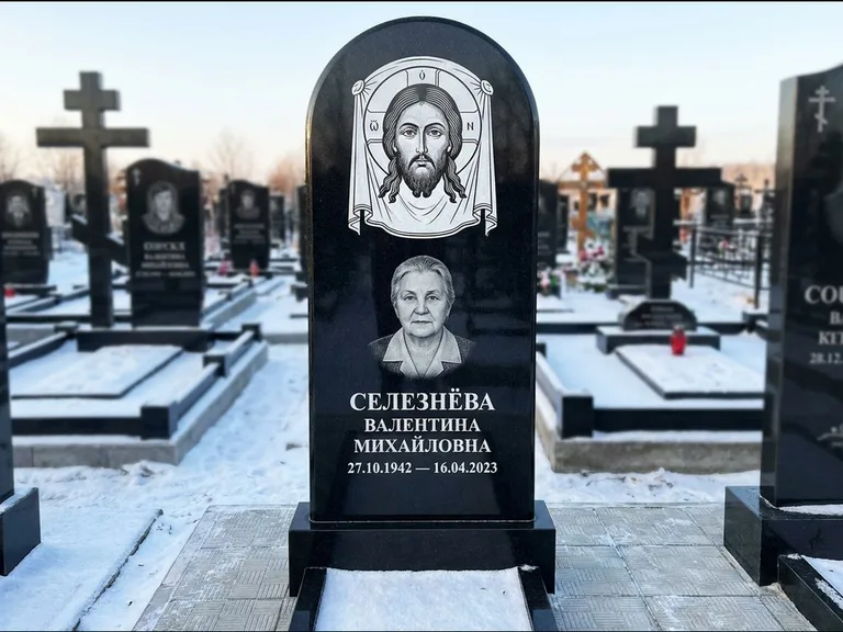 Памятник с гравировкой иконы: небольшая скромная одиночная стела с именной иконой — золочёный нимб на образе, аккуратный участок с газоном, работа «Ковалёв» в Омске