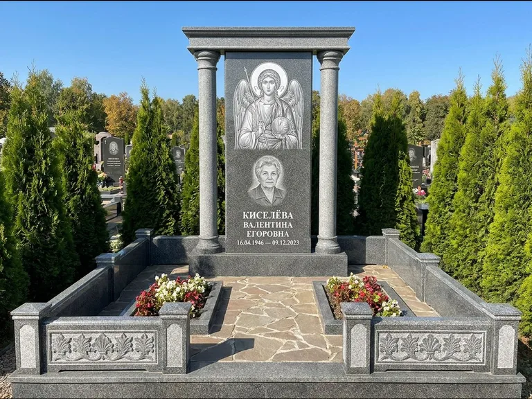 Памятник с гравировкой иконы: массивная стела с двускатным навершием-домиком — гравировка Николая Чудотворца, живая изгородь из туи, работа «Журавлёв» в Омске