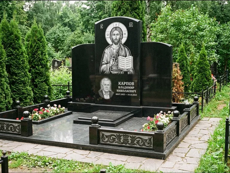 Памятник с гравировкой иконы: широкая панорамная стела с золочёным нимбом — гравировка образа Матроны Московской, цветник с белыми хризантемами, работа «Мельникова» в Омске