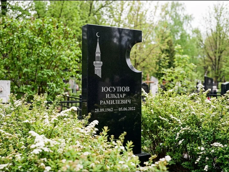 Мусульманский памятник с гравировкой мечети: стела с боковым вырезом в форме полумесяца — гравировка минарета с полумесяцем, низкие кусты спиреи в цвету, работа «Юсупов» в Омске