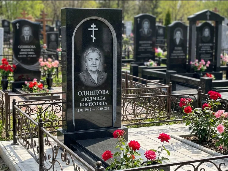 Памятник из чёрного гранита — скромная невысокая стела с крестом с терновым венцом, работа «Лаврентьева» в Омске